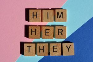 Blocks spelling out different preferred pronouns on a pink, teal and blue background.